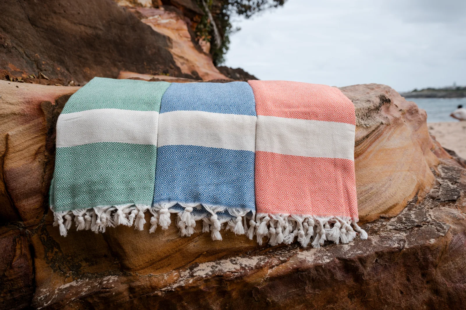 Three colourful foutas arranged on coastal sandstone